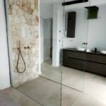 Baño reformado con ducha de obra, mampara de vidrio y pared de piedra en Mallorca