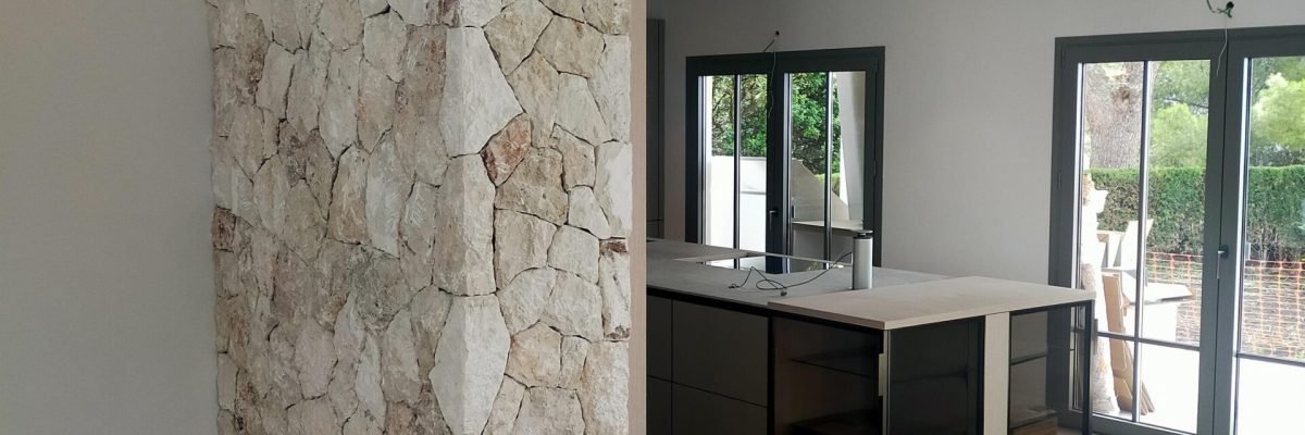 Cocina reformada con isla y pared de piedra en una vivienda de Mallorca